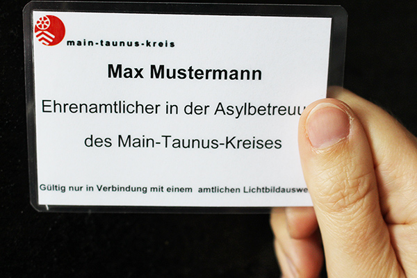 eine Hand, die eine Muster-Ausweiskarte für das Ehrenamt Asylbetreuung hoch hält.