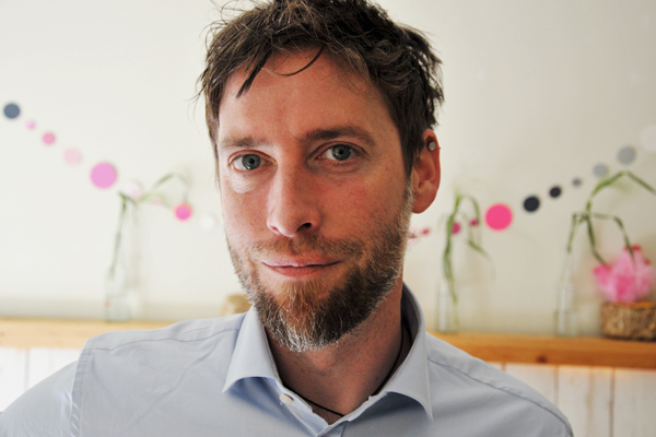 das Portrait eines Mannes mit Bart in einem Raum mit einer bunten Girlande im Hintergrund