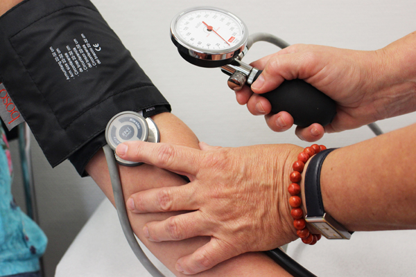 den Arm eines Menschen, dem gerade von einer anderen Person der Blutdruck gemessen wird.