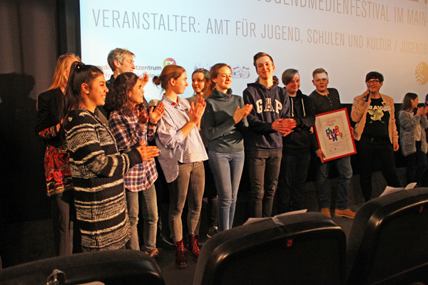 eine Gruppe applaudierender Jugendlicher vor einer Leinwand
