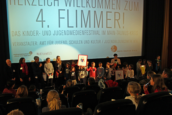 eine Gruppe Kinder, die vor Publikum in einem Kinosaal steht