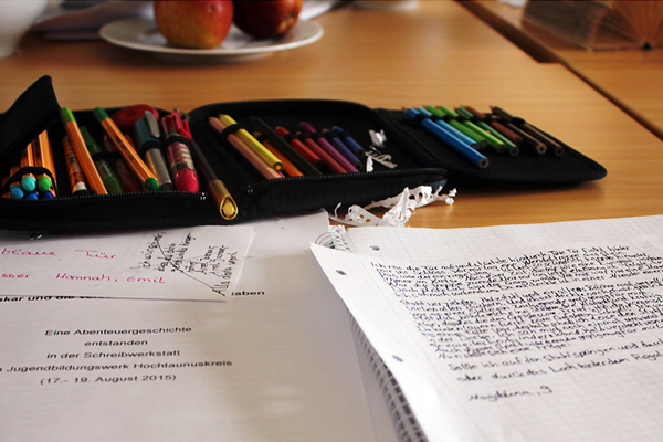 ein Mäppchen mit bunten Stiften auf einem Tisch, davor ein beschriebenes Blatt Papier