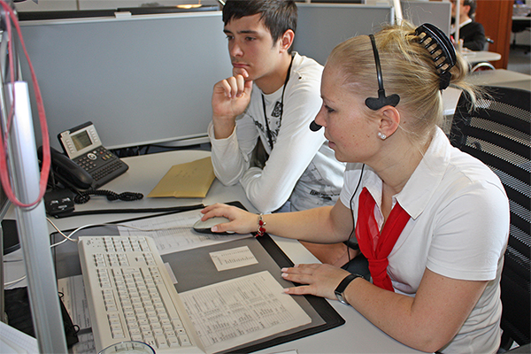 eine junge Frau am Computer. Ein Jugendlicher schaut ihr bei der Arbeit zu.