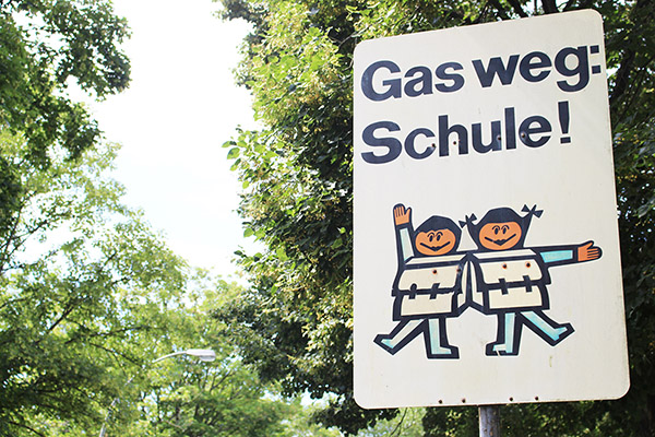 ein Schild mit zwei Kindern, die einen Schulranzen tragen. Darüber steht die Schrift Gas weg: Schule!