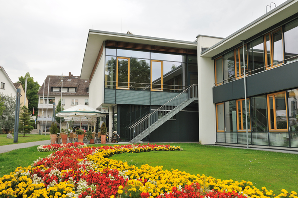 ein großes Gebäude mit verglaster Fassade hinter einer Wiese mit einem bunten Blumenbeet.