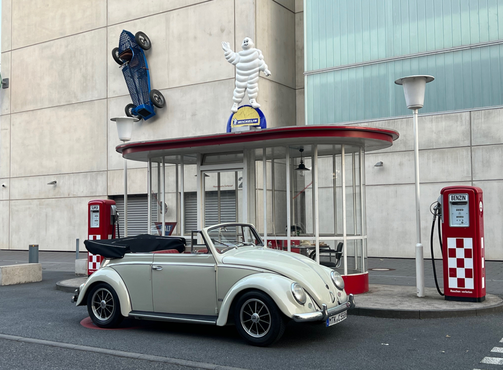 Cremefarbenes Cabrio vor einer alten Tankstelle, mit einem Automodell, das an einer WAnd hängt | Copyright: Teilnehmer Cremefarbenes Cabrio vor einer alten Tankstelle, mit einem Automodell, das an einer WAnd hängt