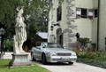 Silberfarbenes Cabriolet vor einem Anwesen, im Vordergrund eine Statuette | Silberfarbenes Cabriolet vor einem Anwesen, im Vordergrund eine Statuette