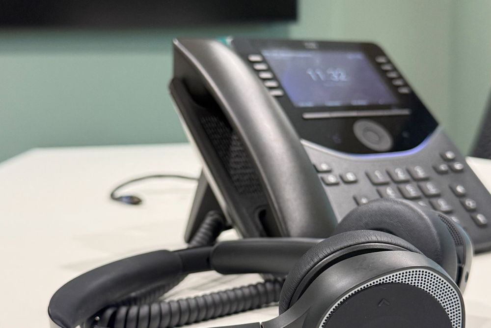 Ein Kabeltelefon und ein Headset liegen auf einem Schreibtisch