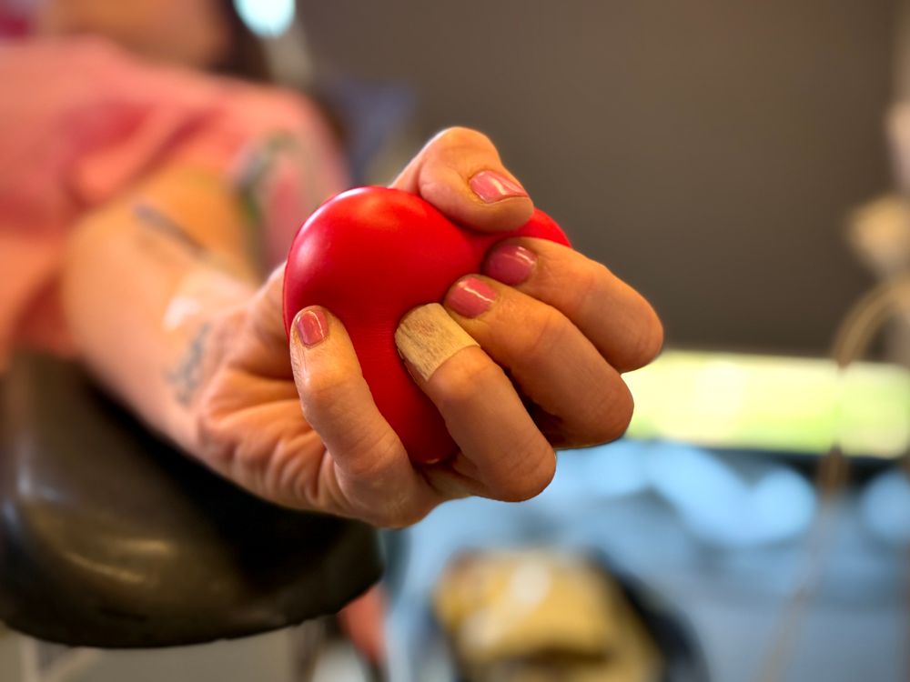 Eine Frau bei der Blutspende, die einen roten Ball in Herzoptik in der Hand hält
