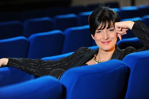 eine Frau sitzt in Abendgarderobe zwischen blauen Kinosesseln
