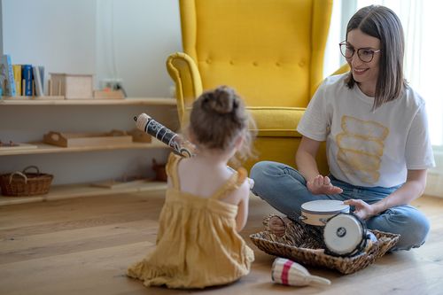 eine juinge Frau mit Brille musiziert mit Holzinstrumenten mit einem Kleinkind
