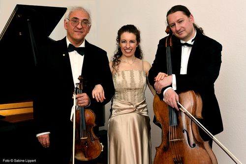 ein Trio mit Instrumenten vor einem Klavier
