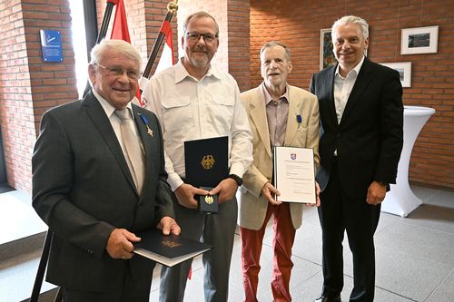 vier Männer, drei davon halten Ehrenurkunden und haben Verdienstorden
