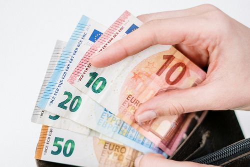 Ein Symbolbild mit mehreren Euro-Scheinen, einer Geldbörse und einer Hand, die beides hält.
