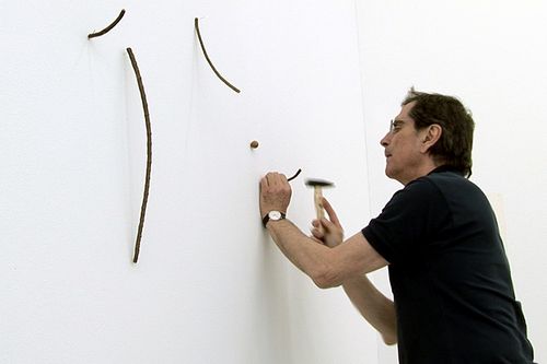 ein Mann mit Brille nagelt Seilstücke an eine Wand
