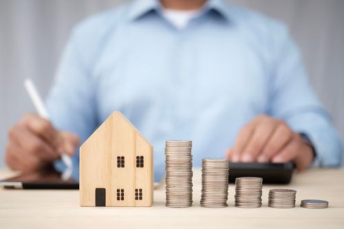 symbolisches Haus neben gestapeltem Geld
