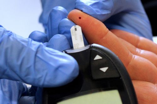 Finger mit Blutstropfen bei einer Blutzuckermessung mit Messgerät
