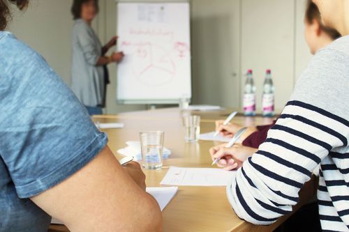Drei Frauen sitzen am Schreibtisch und hören sich einen Vortrag an
