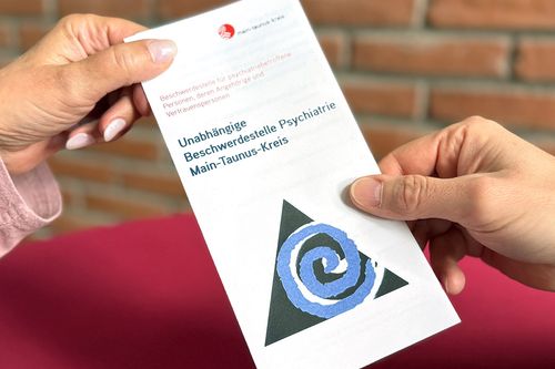 Zwei Hände halten den Flyer der Beschwerdestelle Psychatrie des Main-Taunus-Kreis
