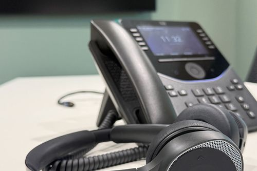 Ein Kabeltelefon und ein Headset liegen auf einem Schreibtisch
