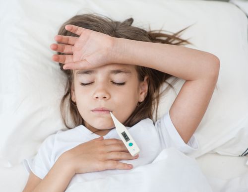 Ein Kind liegt mit Fieberthermometer im Bett 