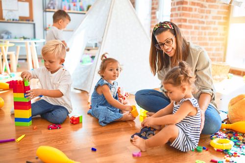 Eine Frau speilt mit vier Kindern mit bunten Bauklötzen