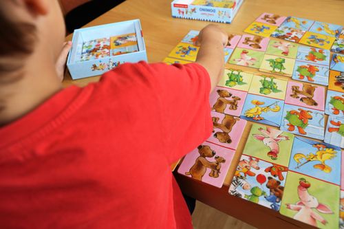 Ein Kind legt bunte Tierkarten eines Domino-Spiels auf einem Tisch aus